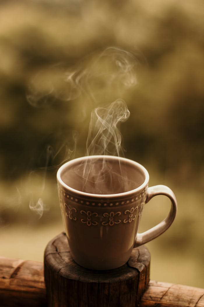 about-01 A steaming coffee mug sits on a wooden surface, emitting gentle steam in an atmospheric outdoor setting.